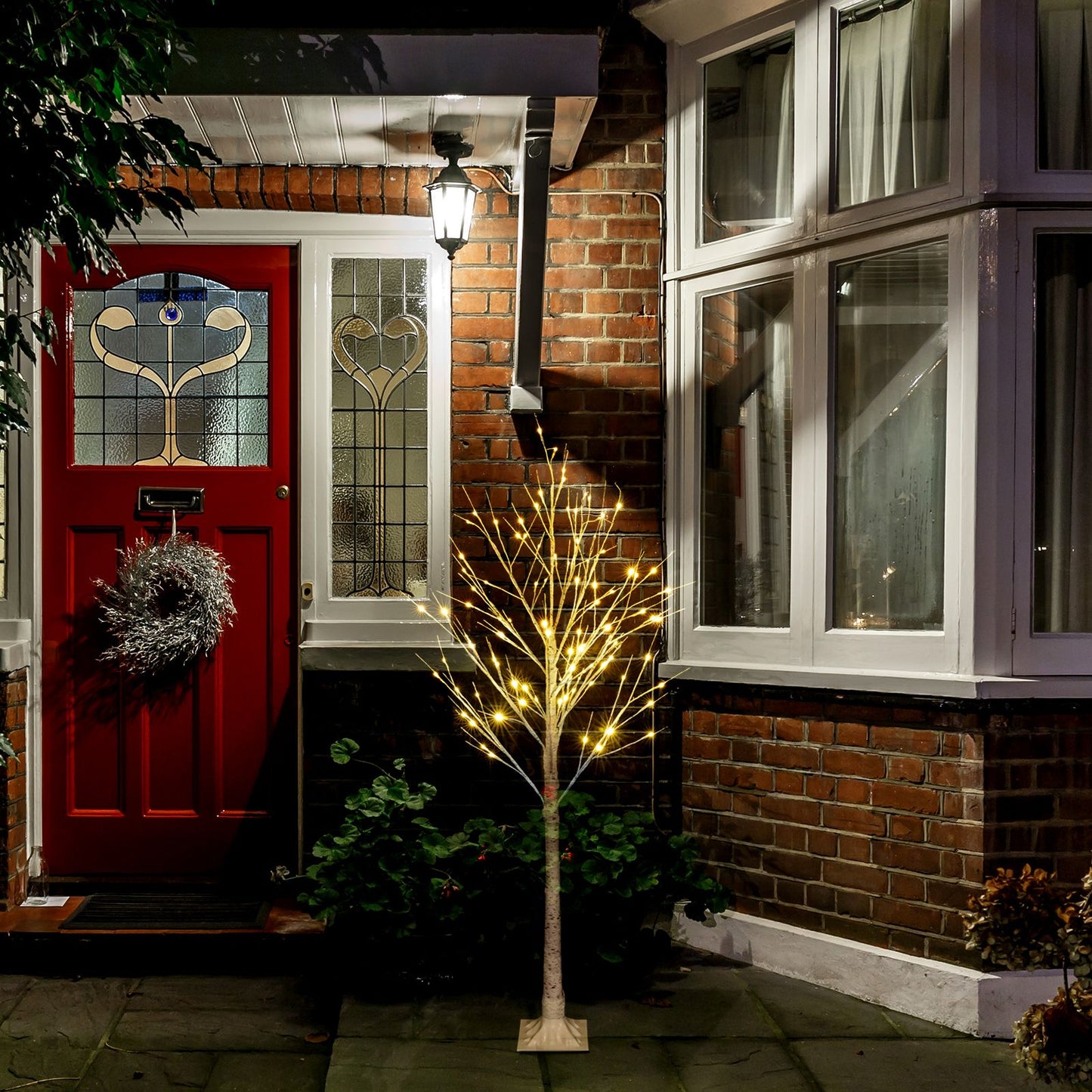 4ft snowflake Christmas tree with lights illuminated outside a brick house near a red door