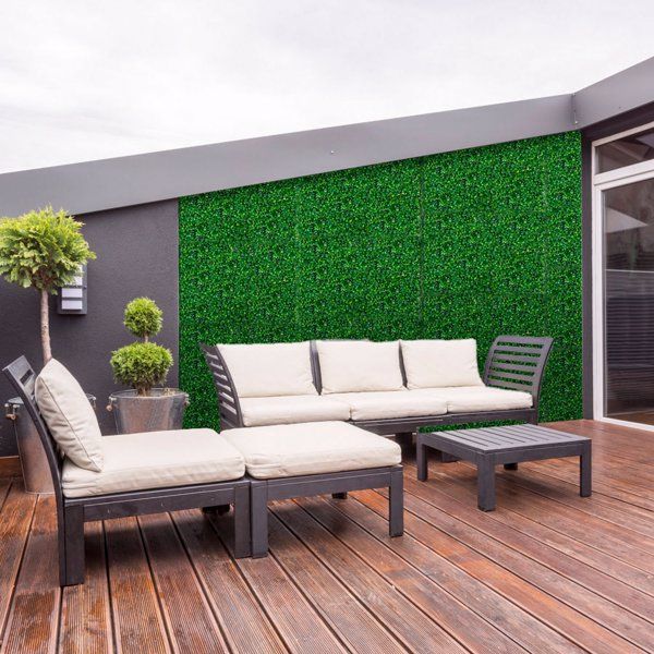 Artificial boxwood hedge panels used as a decorative wall on a modern patio with outdoor furniture