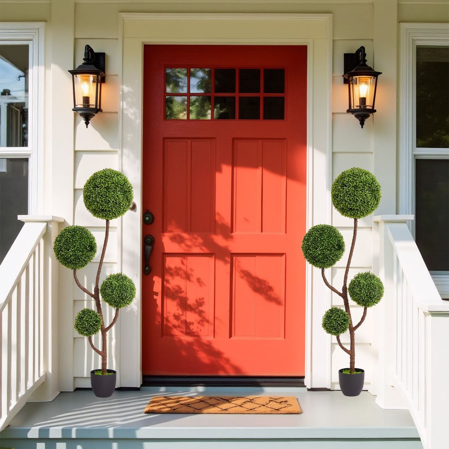 Two artificial boxwood topiary trees in black pots flanking a vibrant red front door