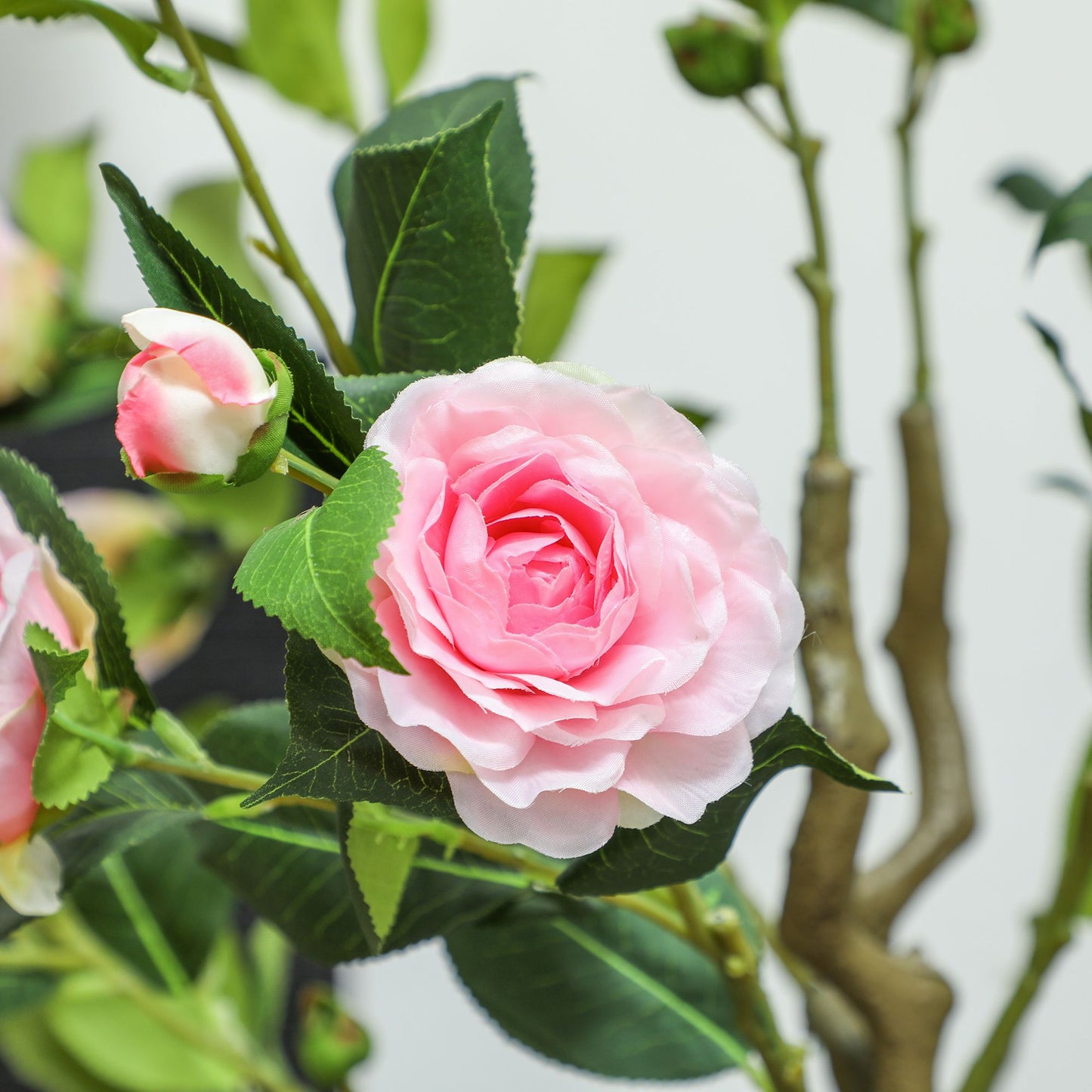 Close-up of pink artificial camellia flowers in pots with green leaves and stems from FauxMart.com