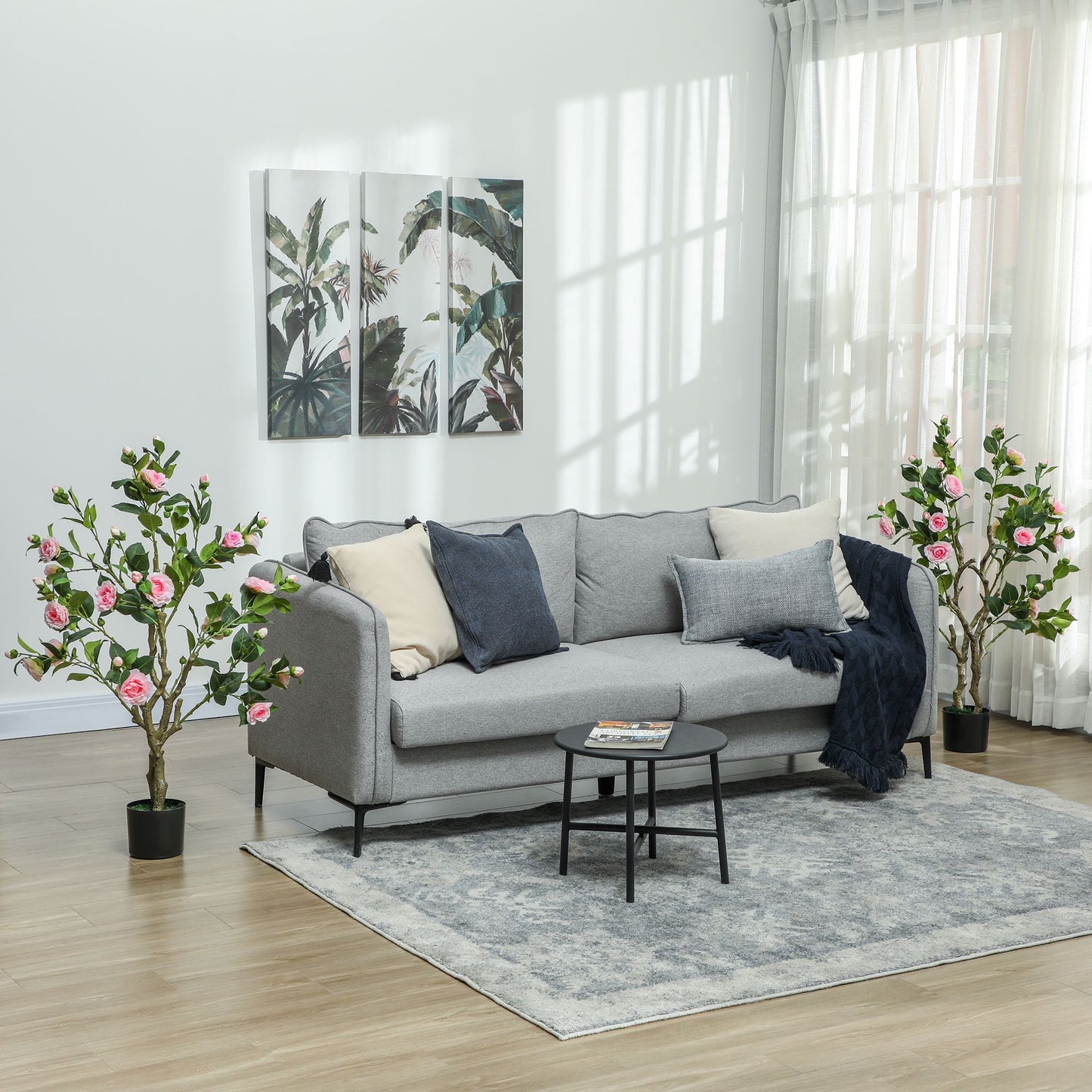 Artificial camellia flowers in pots placed on either side of a modern gray sofa in a bright living room