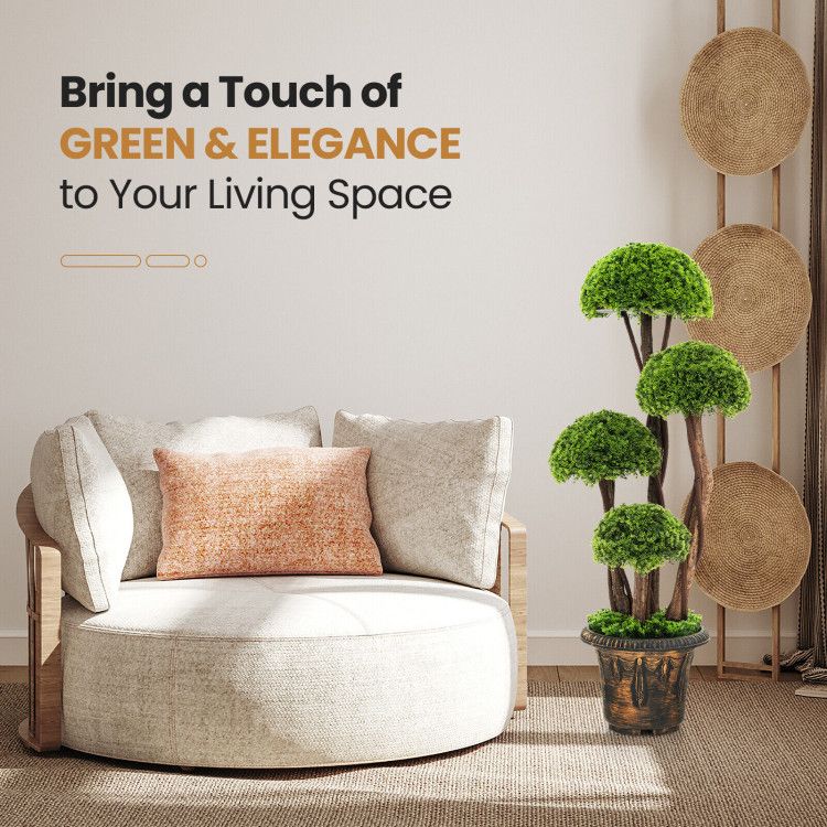 Artificial cedar topiary tree with layered green foliage in a decorative pot beside a beige modern chair