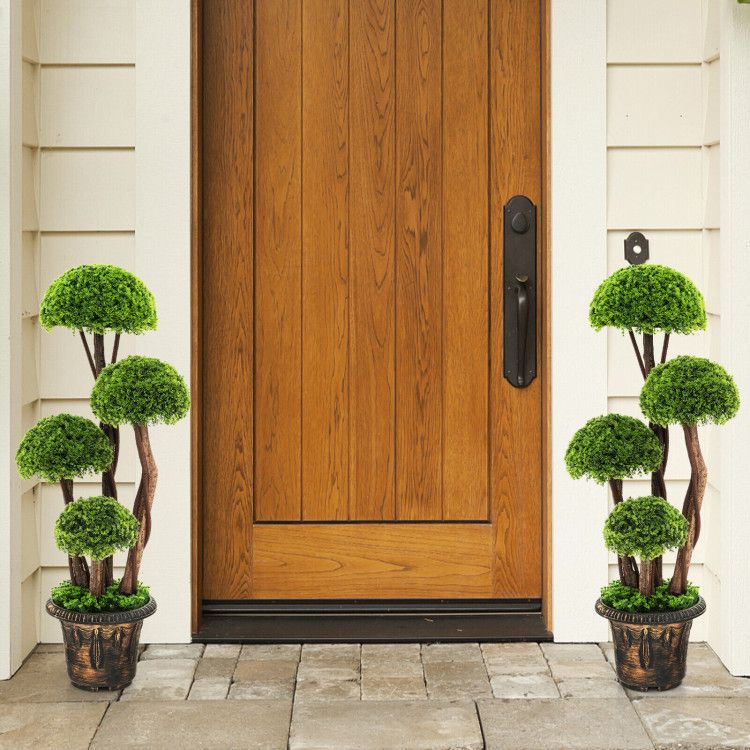 Pair of artificial cedar topiary tree plants in decorative pots placed beside a wooden front door