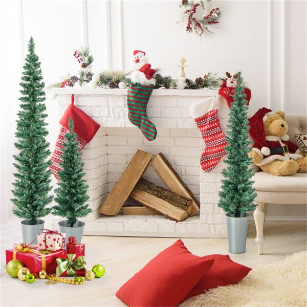Artificial Christmas trees set in decorative pots near a cozy fireplace with holiday decorations