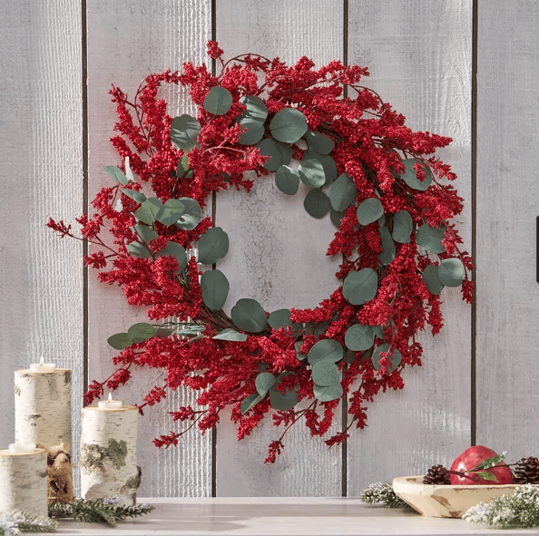 Artificial Christmas wreath with eucalyptus and red berries hanging on white wooden wall
