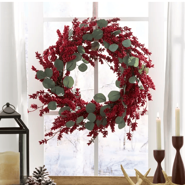 Artificial Christmas wreath with eucalyptus and red berries hanging on a window with holiday decor