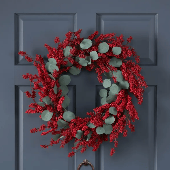 Artificial Christmas wreath with eucalyptus and red berry branches hanging on a dark gray door