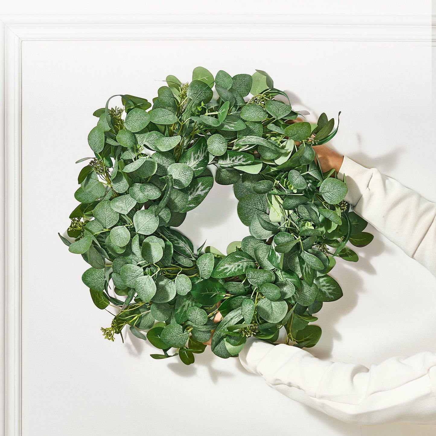 Artificial eucalyptus wreath with lush green leaves held by hands against white background