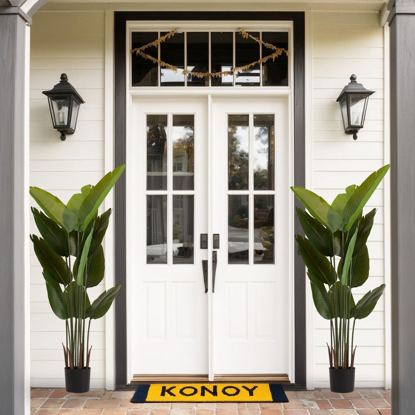 Two tall artificial green plant set in black pots near a white front door with decorative lighting