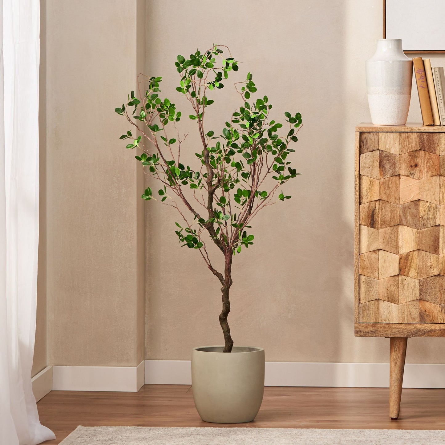Artificial Milan leaf bonsai tree in modern beige pot placed in a stylish living room corner by wooden cabinet