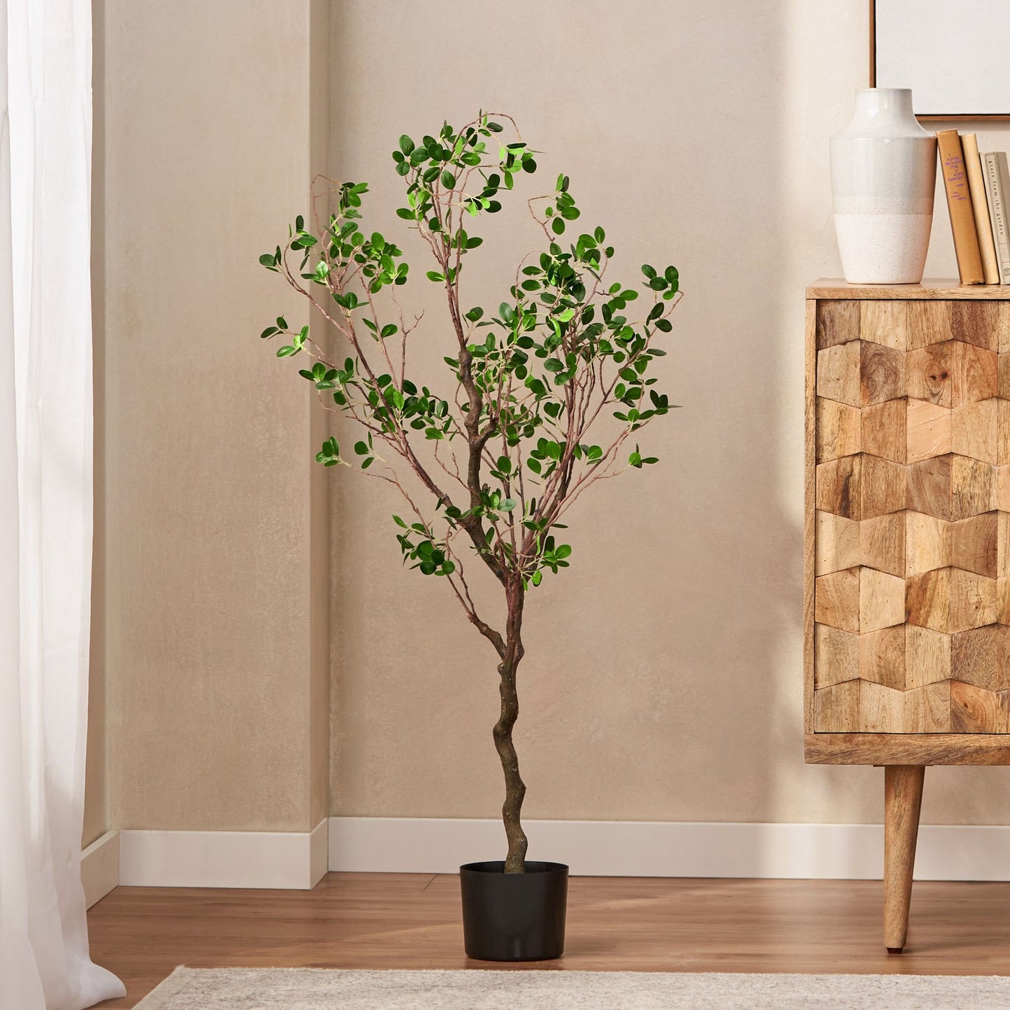 Tall artificial Milan leaf bonsai tree in black pot placed in modern living room corner