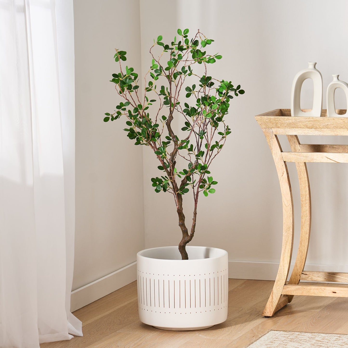 Artificial Milan leaf bonsai tree in white decorative pot next to wooden console table in modern room