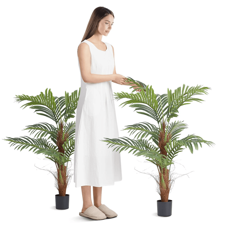 Woman tending to two 4 foot artificial palm trees in stylish planters for home decor.