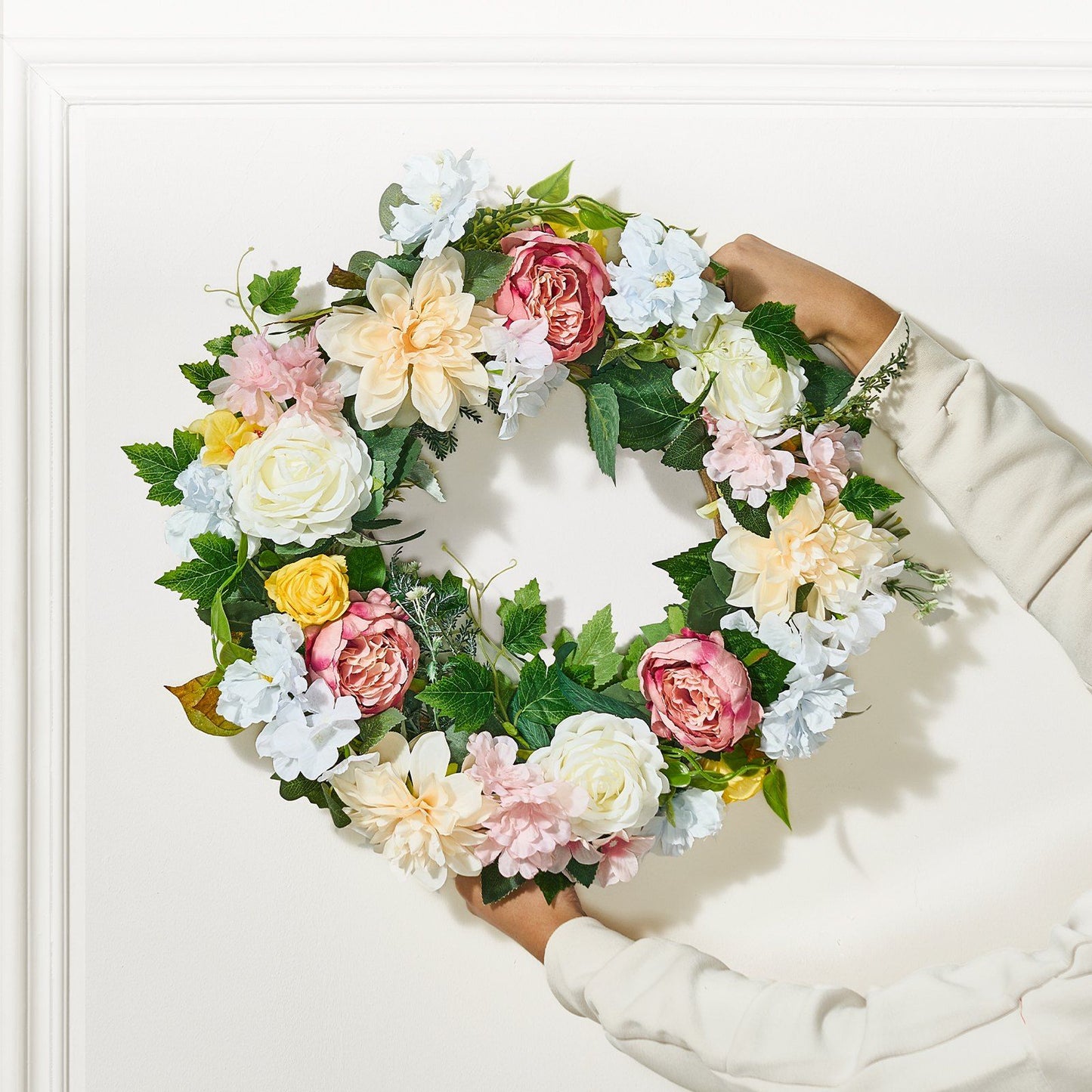 Person holding artificial peony hydrangea wreath with colorful flowers and green leaves
