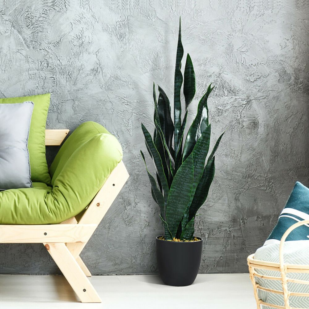Tall artificial snake plant decor in a black pot beside a green chair in a modern living room