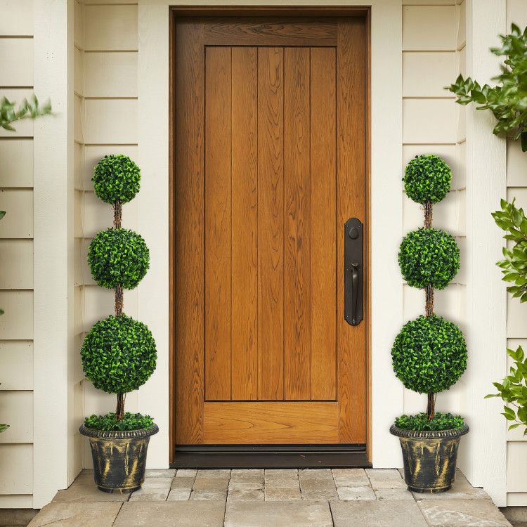 Pair of artificial topiary trees in decorative pots framing a wooden front door entrance