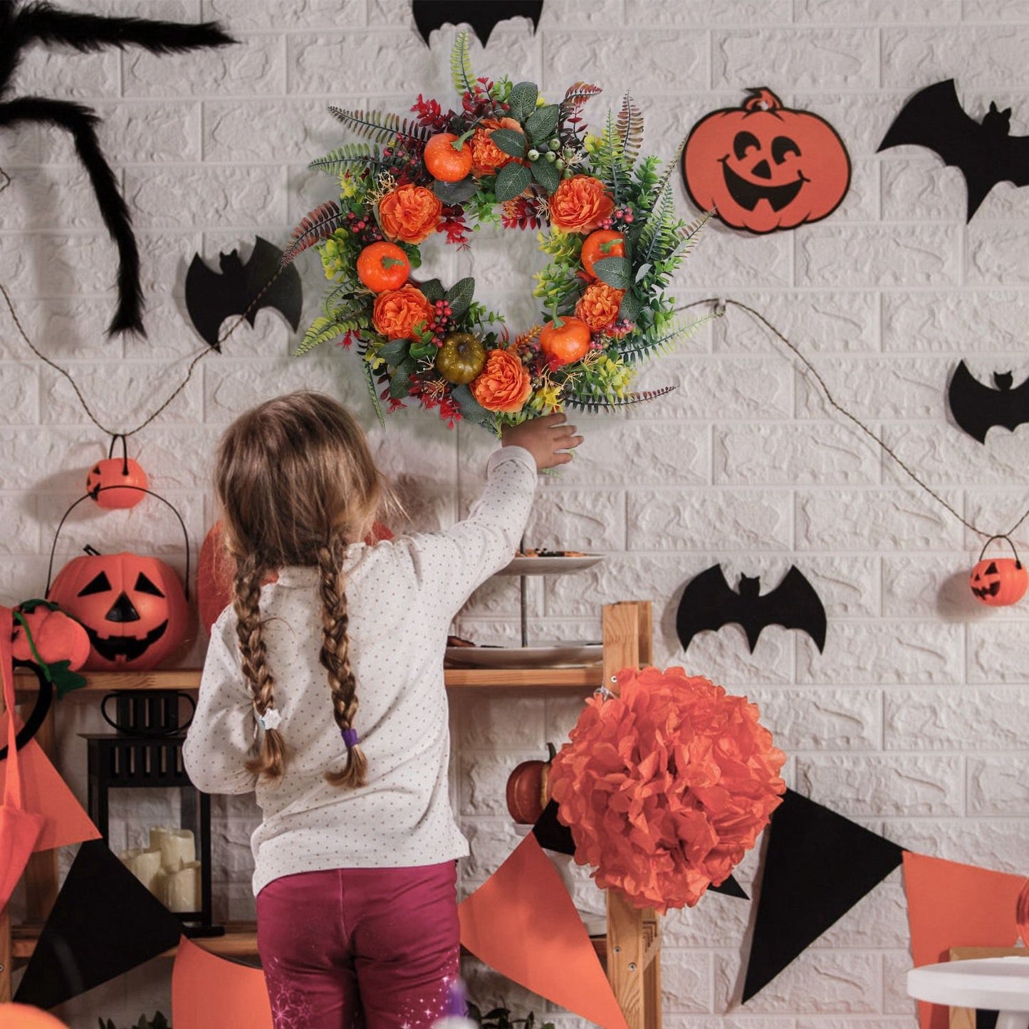 Child hanging an autumn wreath decoration on a wall adorned with Halloween decorations