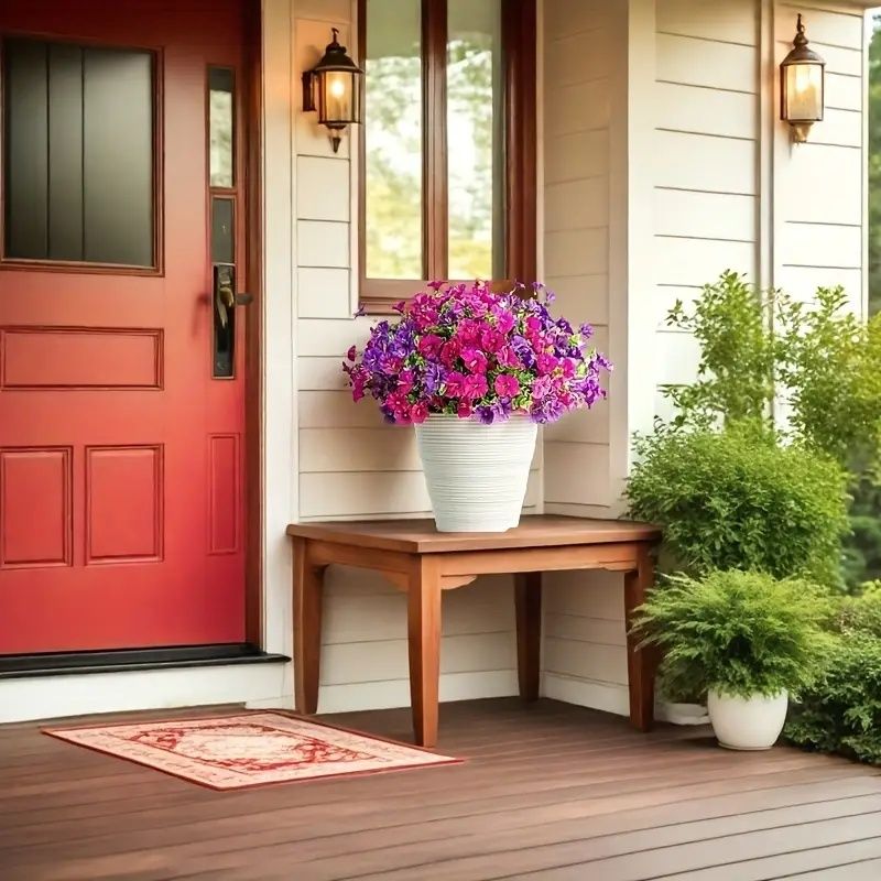 Bright artificial flowers for home in a white pot placed on a wooden table on a front porch