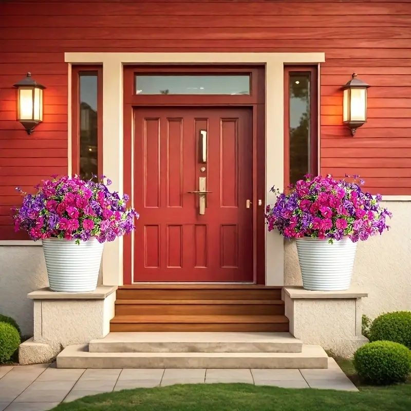Bright artificial flowers for home in white pots flanking red front door on porch steps