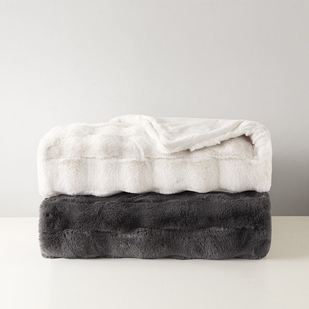 Soft white and dark gray faux fur throw blanket folded and stacked on a white surface