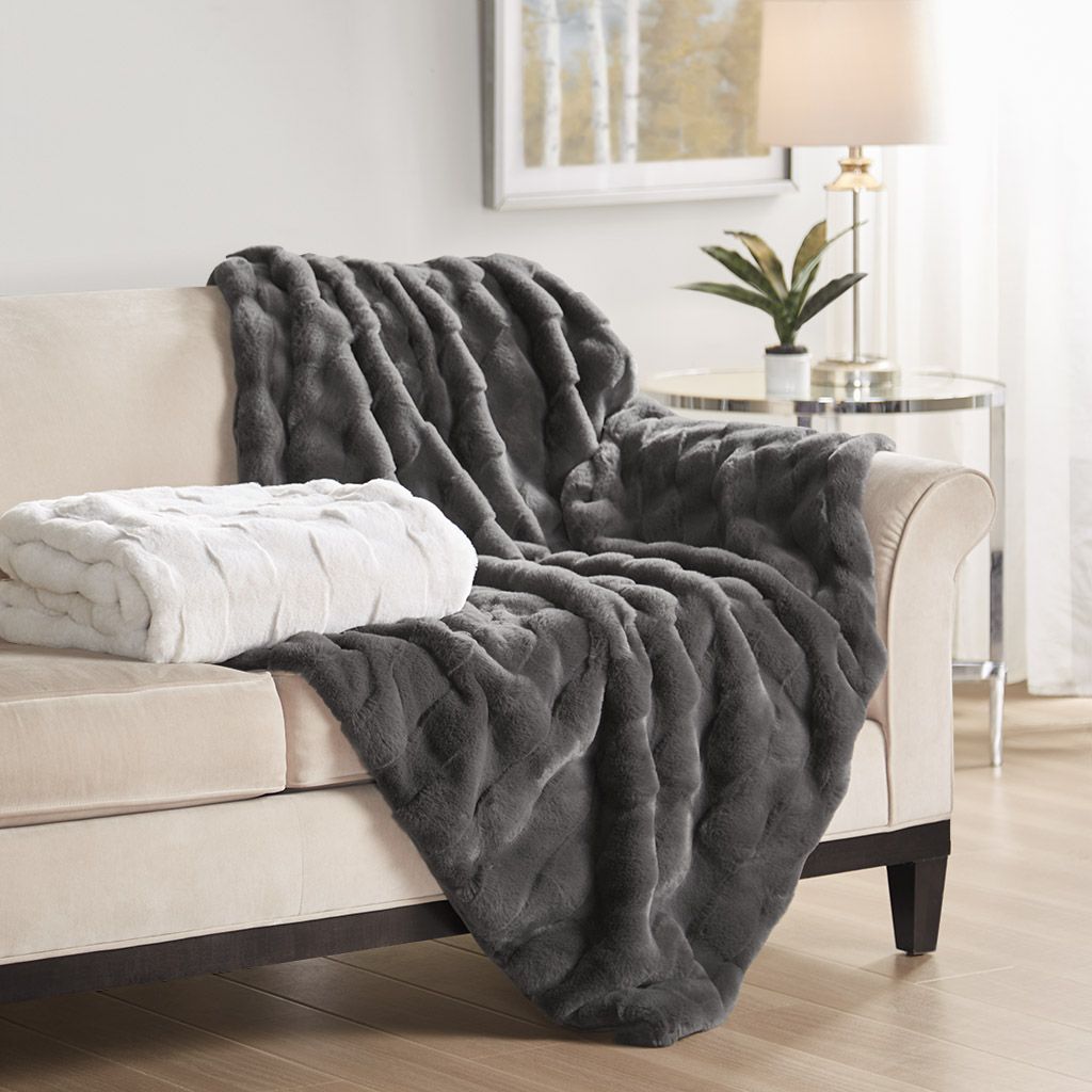 Soft gray and white faux fur throw blanket draped on beige sofa in a modern living room