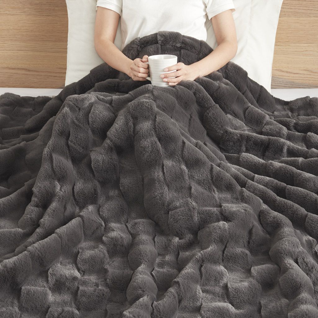 Cozy dark gray faux fur throw blanket from FauxMart.com covering a person holding a white mug in bed