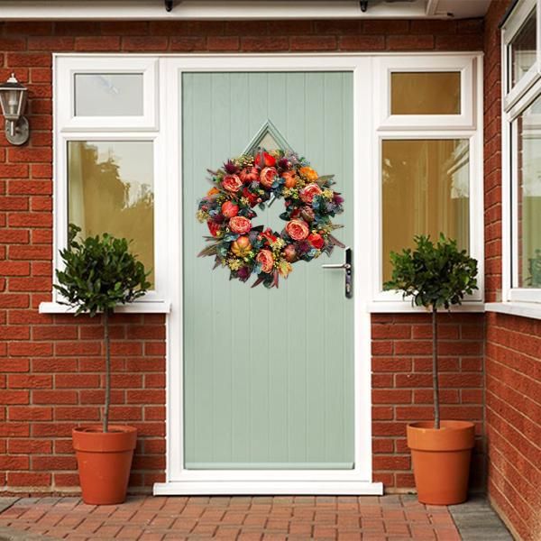 Colorful artificial flower door wreath hanging on a light green front door with brick walls and potted plants