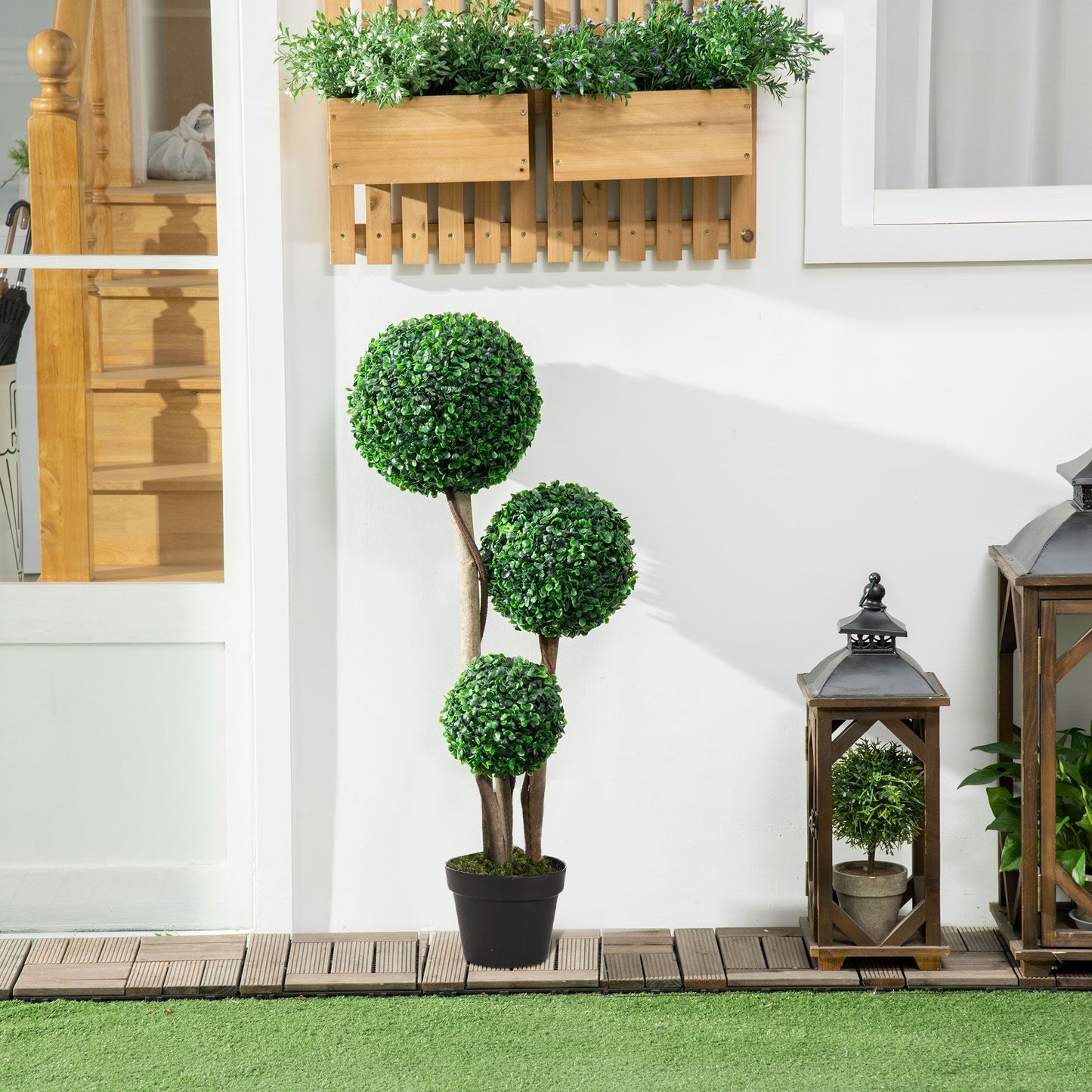 Artificial boxwood topiary tree with three green spheres in black pot placed indoors by wooden decor