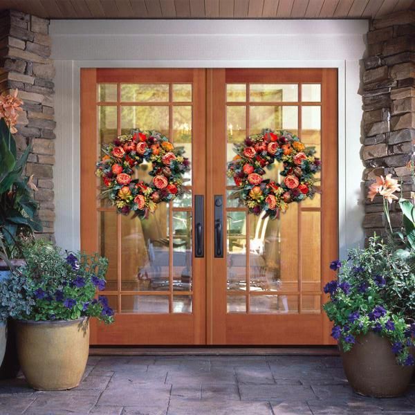 Pair of vibrant artificial flower door wreaths with orange and purple blooms on wooden double doors