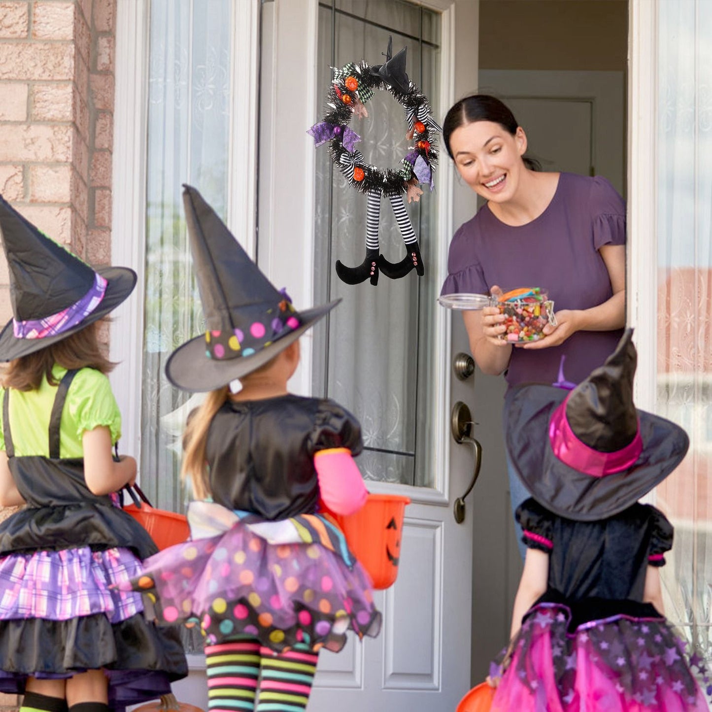 Halloween witch wreath hanging on front door with kids trick or treating in witch costumes