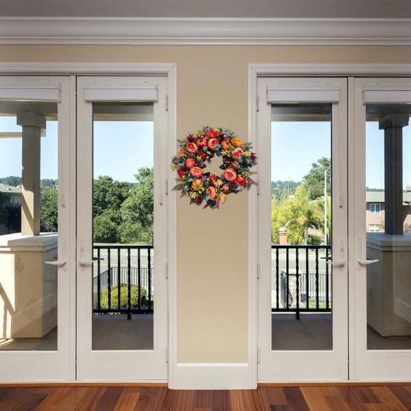 Colorful artificial flower door wreath hanging on cream wall between glass patio doors
