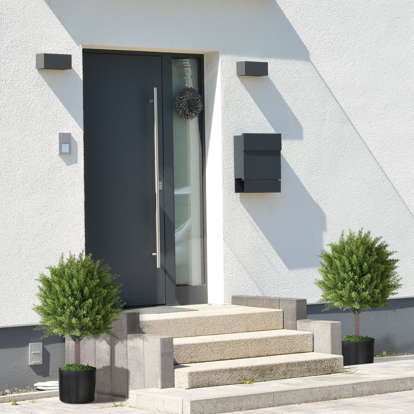 Two green indoor outdoor fake plants in black pots flanking modern house front door steps