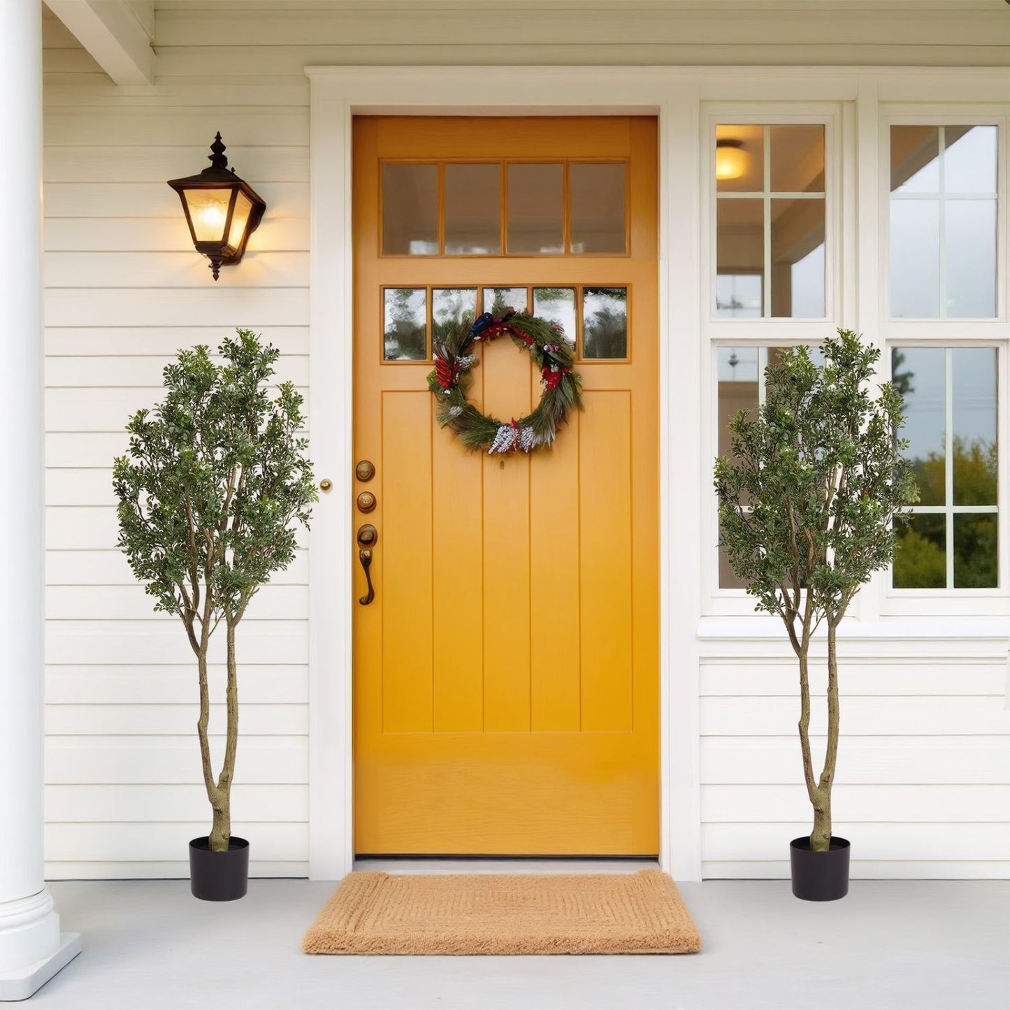 Pair of large artificial plants in black pots by a vibrant yellow front door with a wreath