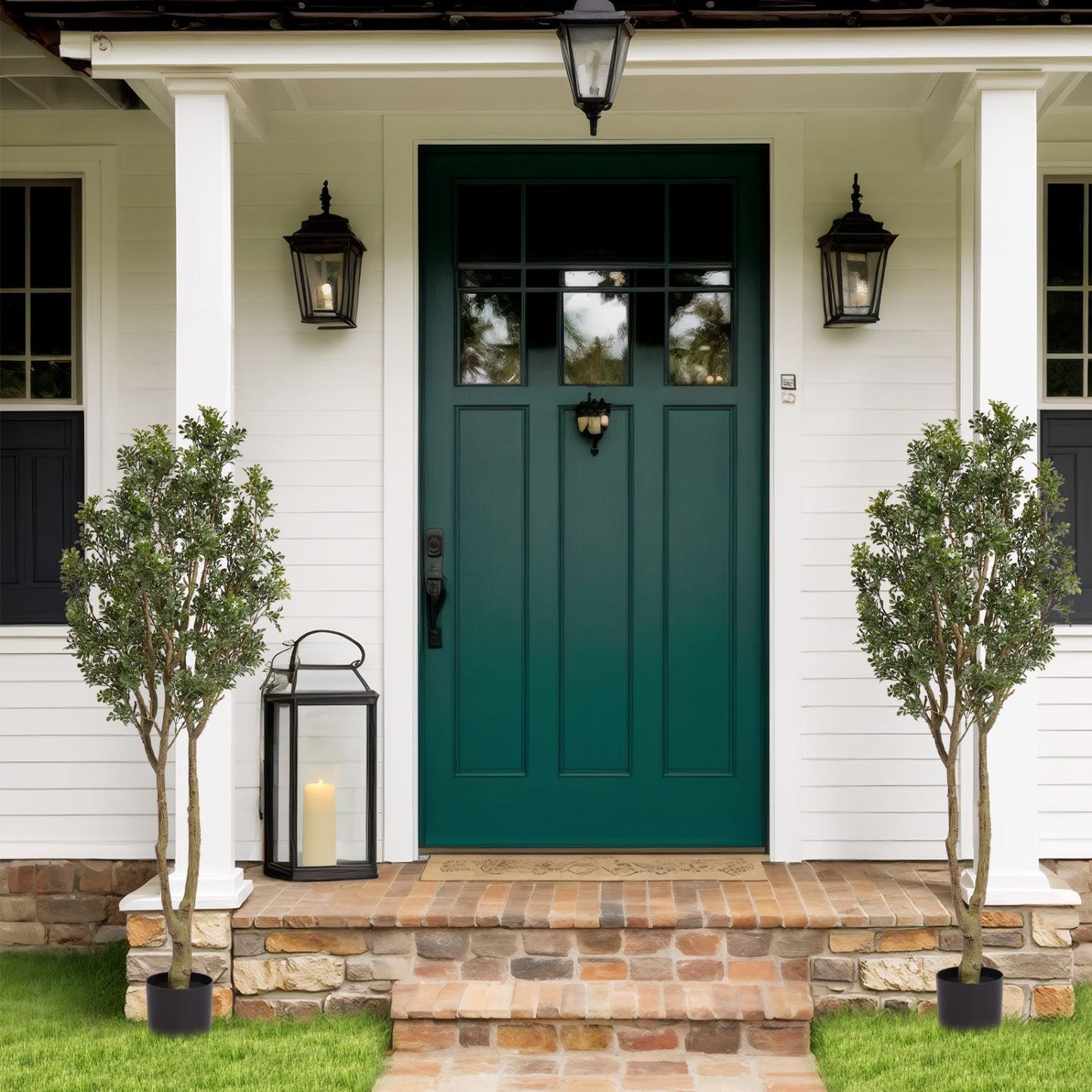 Two large artificial plants in modern black pots flanking a green front door for stylish outdoor decor