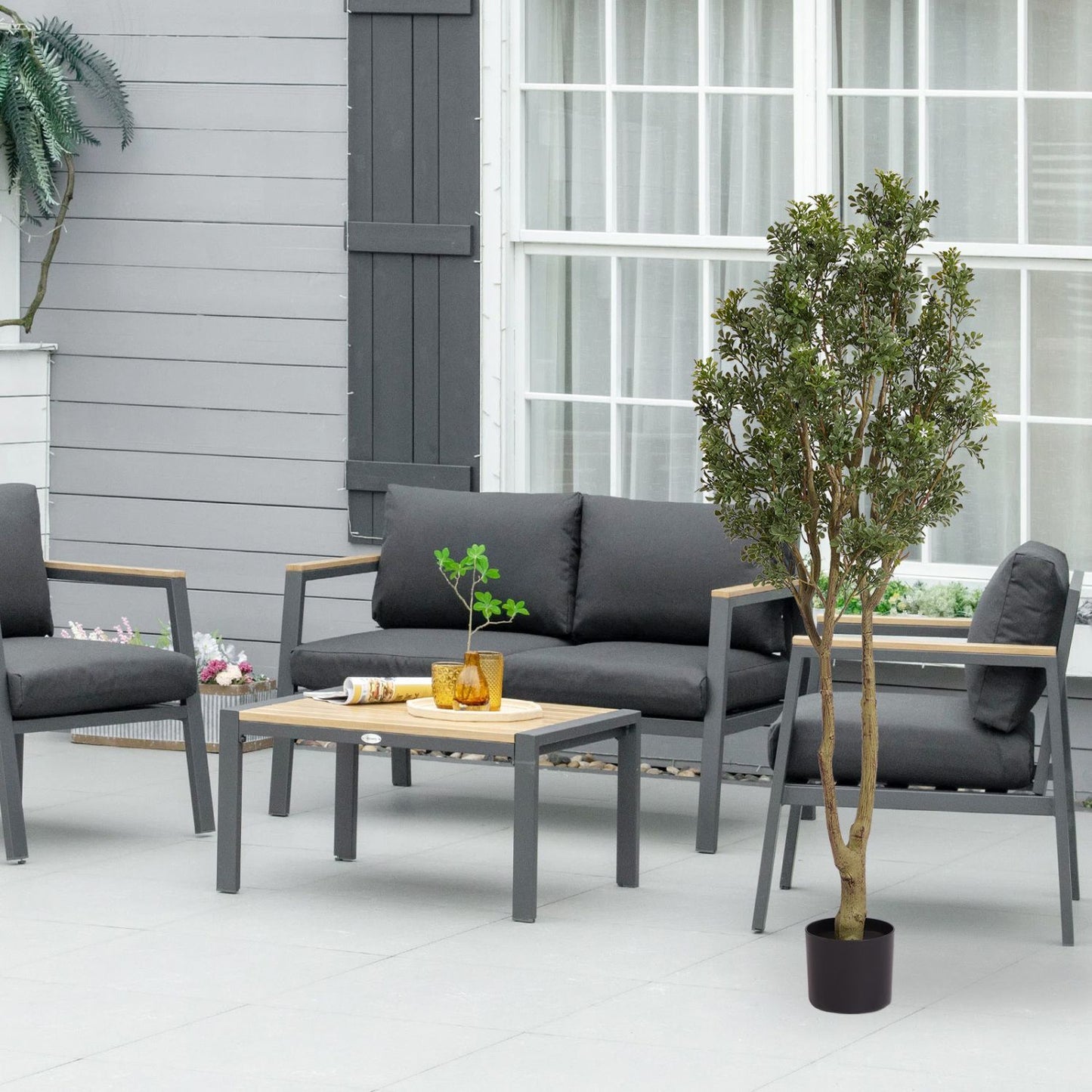 Large artificial plants in a stylish outdoor seating area featuring gray furniture and a wooden coffee table