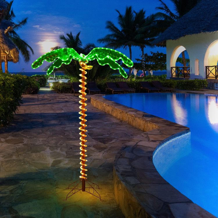 LED palm tree decor illuminated with green leaves and orange trunk by poolside at night