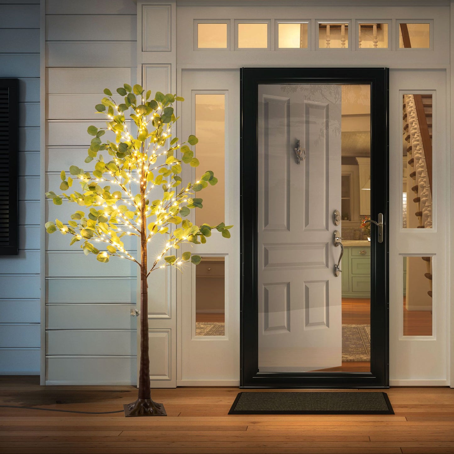 Lighted artificial olive tree with warm white lights by front door on porch at night