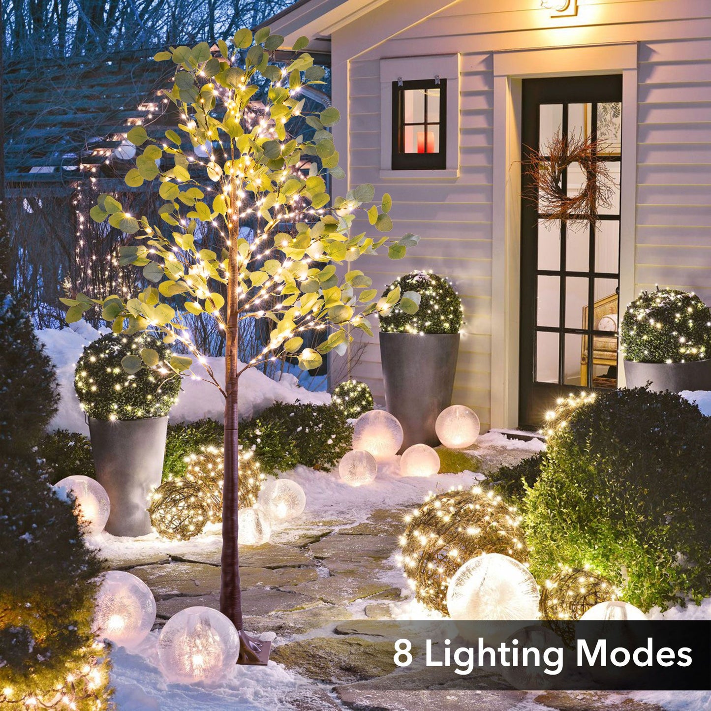 Lighted artificial olive tree with warm white lights displayed outside a house entrance in winter