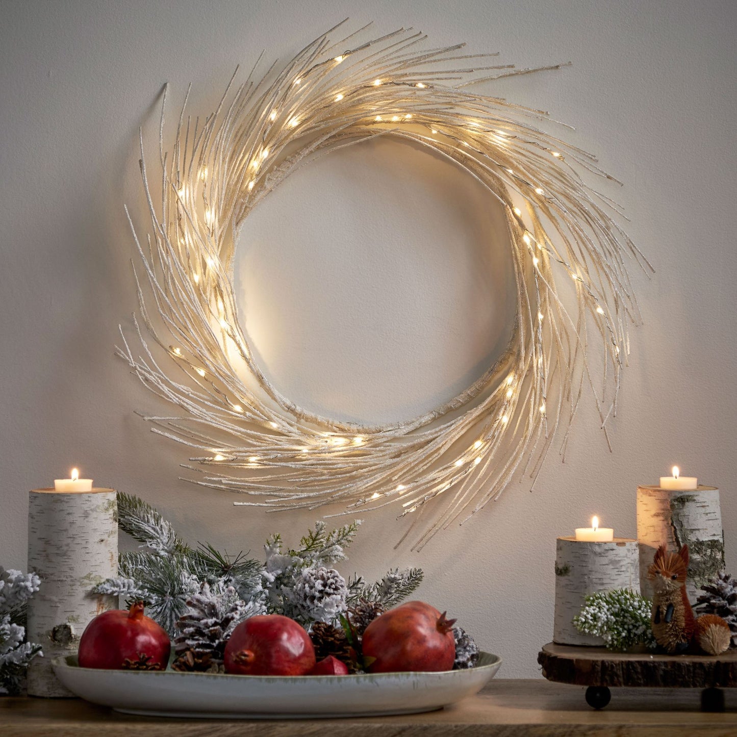 Lighted paper wreath with warm white lights hanging on wall above holiday table decor with candles and pine cones