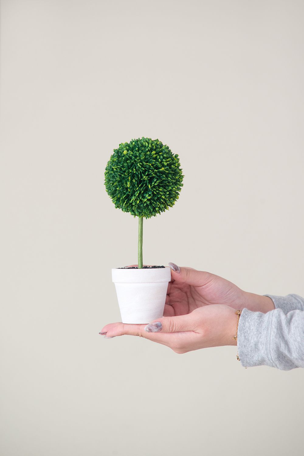Hand holding a small green plant in white pot mini faux topiary set from FauxMart.com