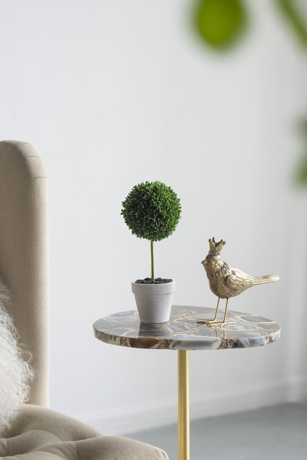 Mini faux topiary set with round green artificial plant in white pot on marble side table