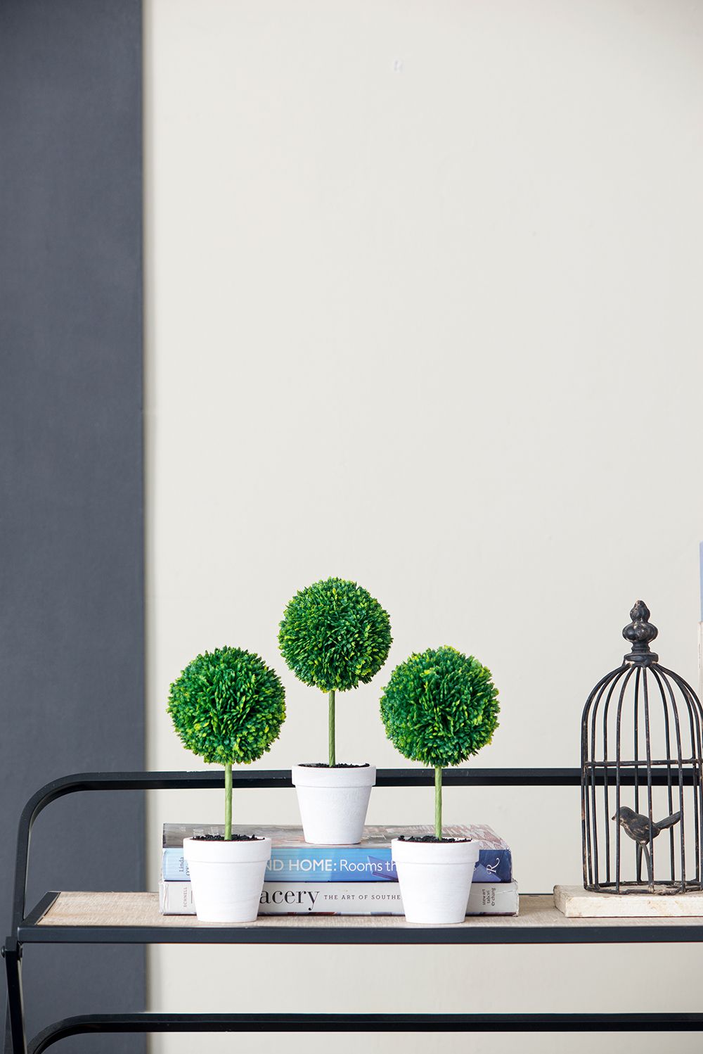 Mini faux topiary set with three green spherical artificial plants in white pots on a black shelf