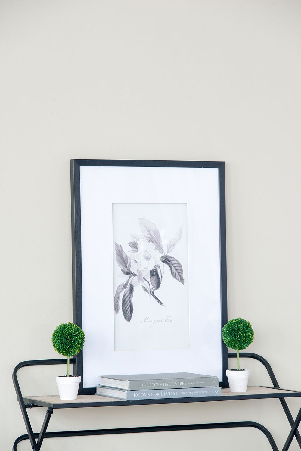 Mini faux topiary set with two small green plants in white pots on black metal table