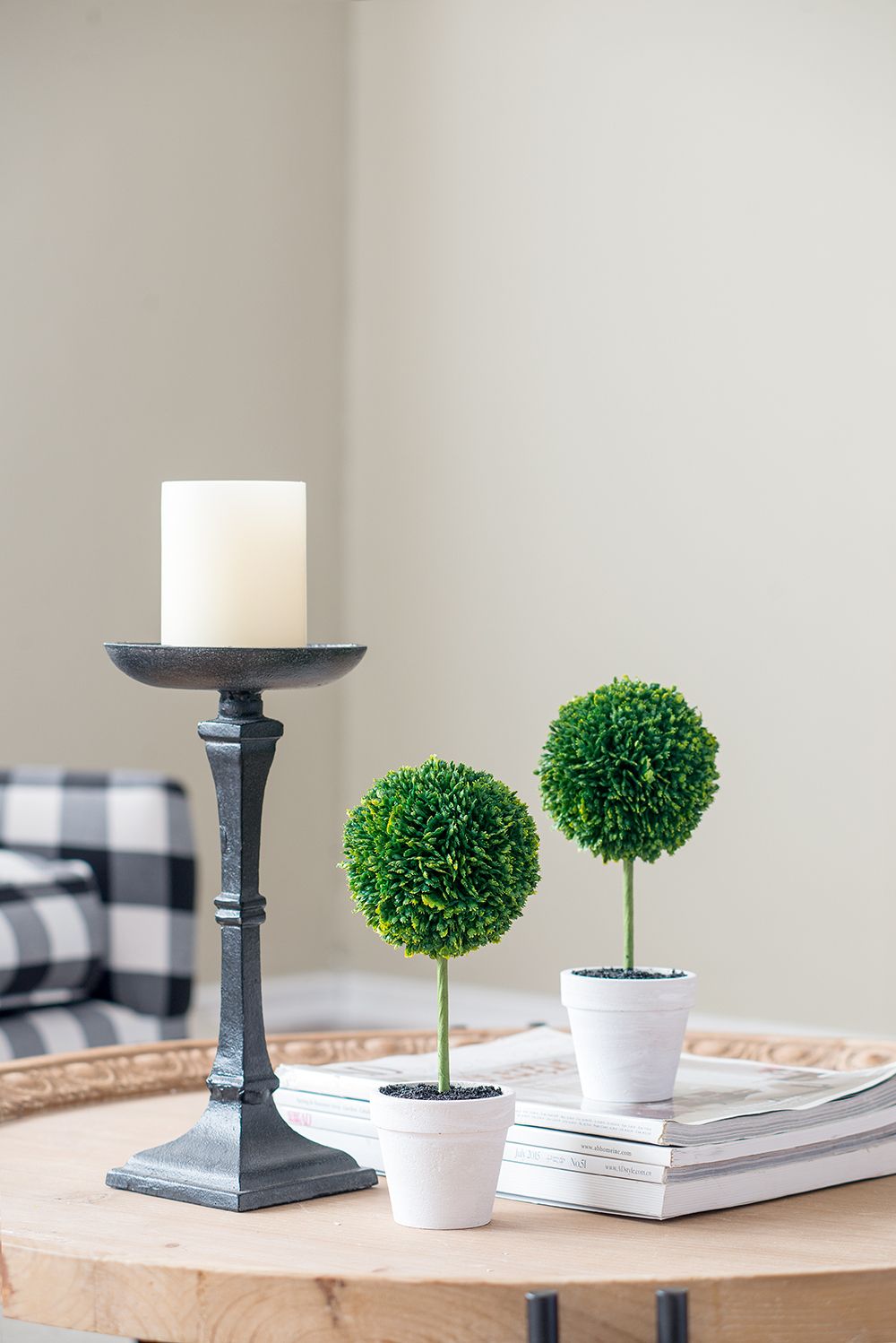 Mini faux topiary set with two green potted plants on a wooden table next to a black candle holder