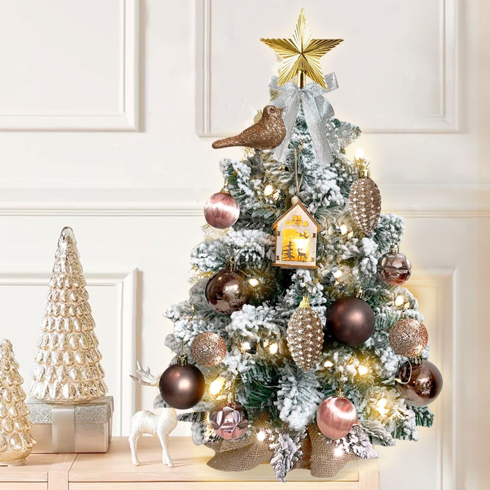 Mini tabletop Christmas tree with lights decorated with gold star, bird, and pink ornaments on white background