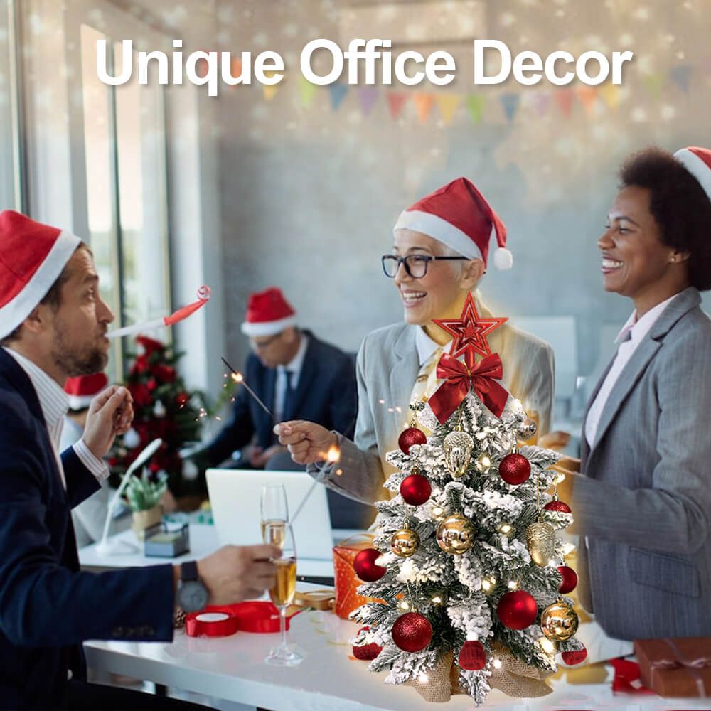 Mini tabletop Christmas tree with lights decorated with red and gold ornaments on office desk with people wearing Santa hats