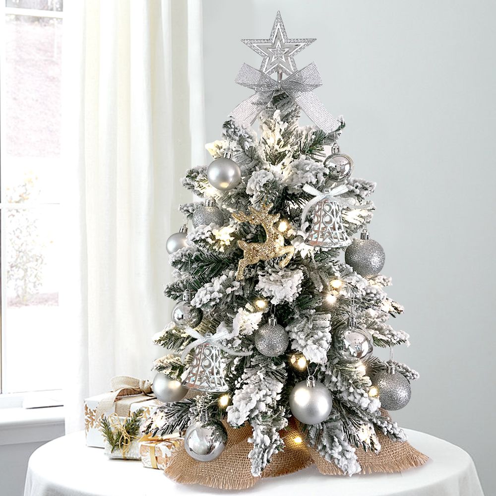 Mini tabletop Christmas tree with lights and silver ornaments on a round white table