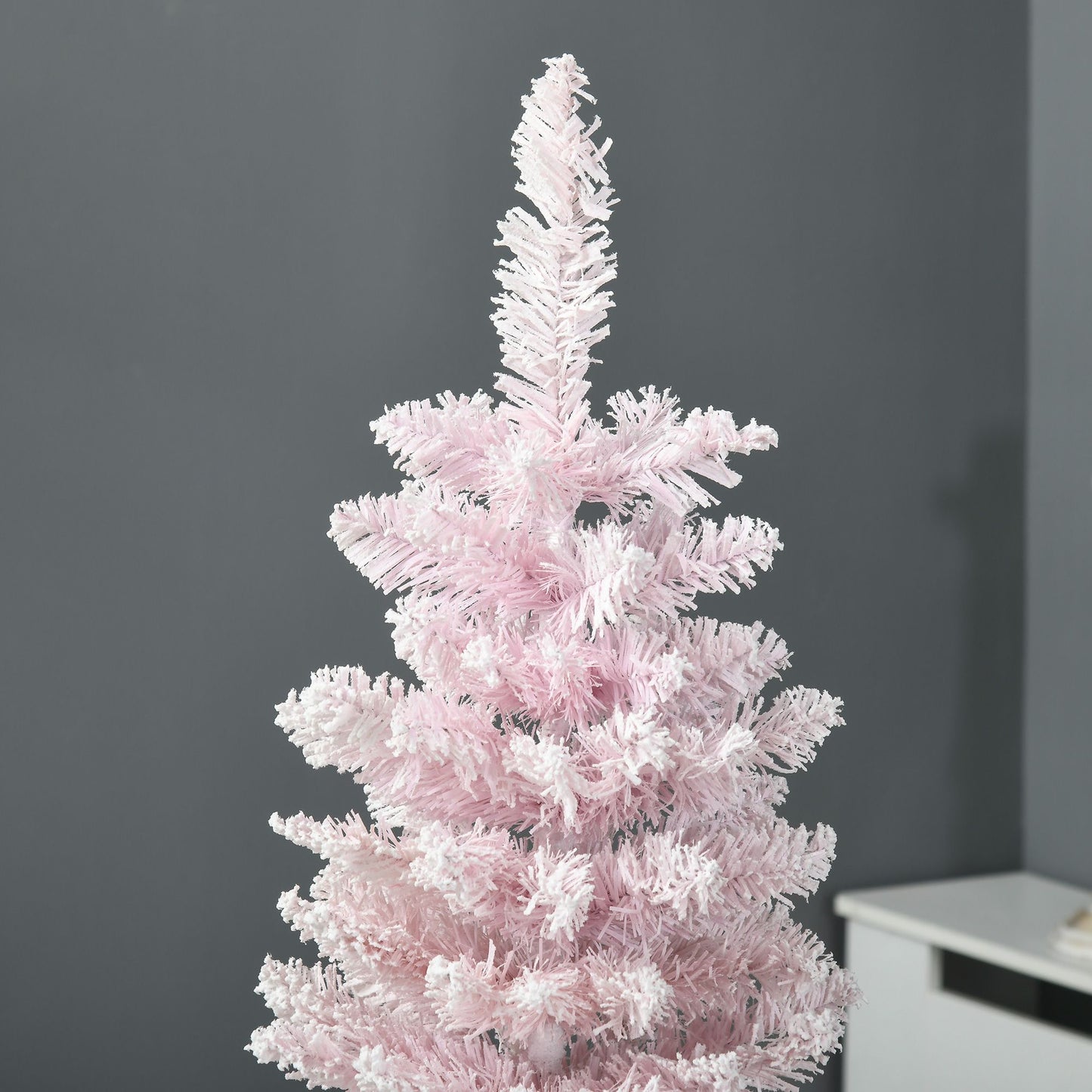 Pink artificial pencil Christmas tree with dense branches against gray wall background