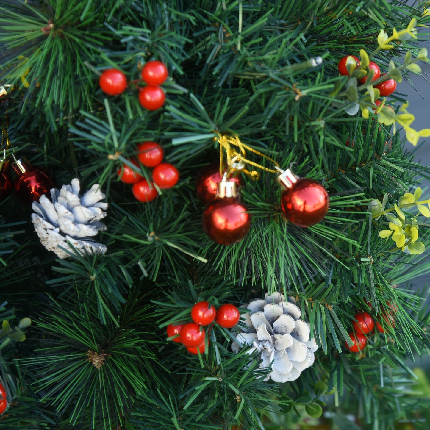 Close-up of pre-lit outdoor Christmas tree set with red berries, pine cones, and red ornaments on green branches
