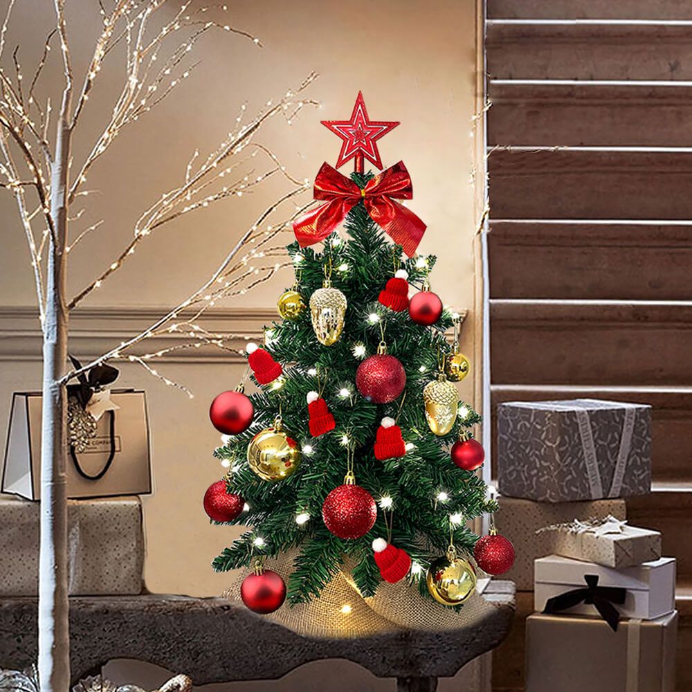 Decorated small Xmas tree for office desk with red bows, ornaments, and warm white lights on a wooden table